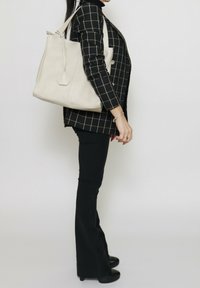 Sac tote en cuir beige avec une forme structurée et une surface texturée, comportant une étiquette hexagonale et une seule sangle pour l'épaule.