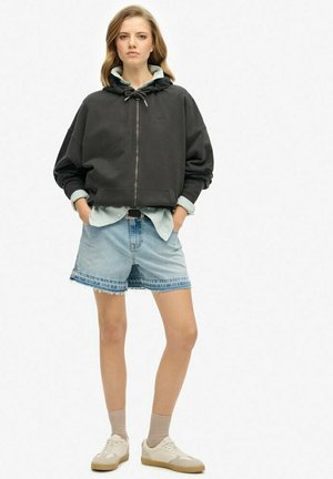 Un hoodie à capuche noir avec cordon et fermeture éclair, associé à une chemise en vichy bleu clair, un short en jean et des baskets beiges.