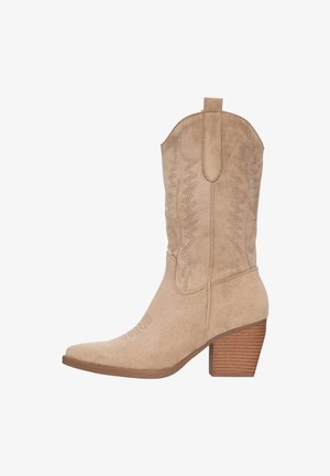 Bottine de cowboy en daim beige avec un bout pointu, une tige haute et des coutures décoratives. Elle présente un talon en bois empilé et une languette en haut.