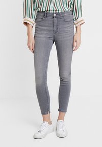 Jeans skinny de denim gris con cintura de altura media, diseño de cinco bolsillos, un ligero desgaste y dobladillo deshilachado, combinados con zapatillas blancas.