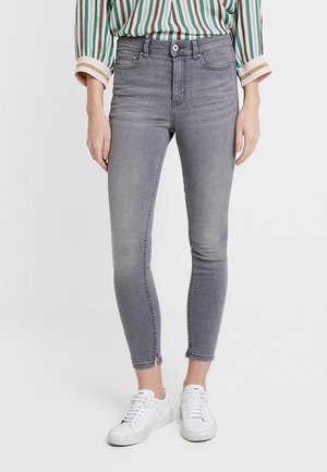 Jeans skinny de denim gris con cintura de altura media, diseño de cinco bolsillos, un ligero desgaste y dobladillo deshilachado, combinados con zapatillas blancas.