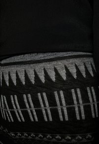 Černá tkanina s šedým vzorovaným pasem s vertikálními pruhy a geometrickými tvary. Textura se zdá být hladká s tkanými akcenty.