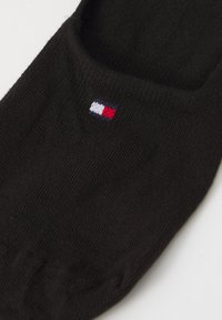 Sosete negre până la glezna, fabricate dintr-un material moale, având un mic logo brodat în culorile roșu, alb și albastru aproape de vârf.