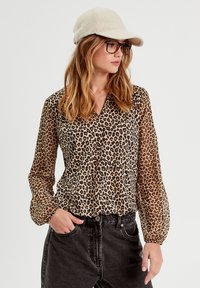 Blusa de estampado de leopardo con mangas largas y transparentes, un frente de botones y un cuello clásico, combinada con jeans negros de cintura alta.