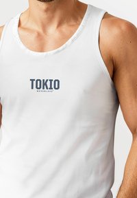 White sleeveless cotton tank top featuring a round neckline and a printed logo "TOKIO NEVERLESS" in dark gray on the front.
