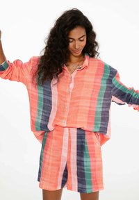 Súprava ľanovej košele a šortiek s širokými pruhmi v ružovej, oranžovej, zelenej a námornej farbe. Voľný strih s gombíkmi na košeli a vreckami na šortkách.