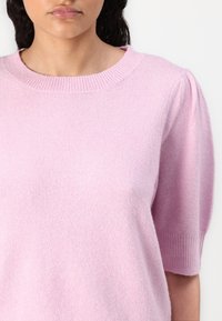 Lichtroze sweater met korte mouwen en een ronde hals, met een zachte, gestructureerde afwerking en subtiele pofdetails op de mouwen.