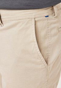 Beige Baumwollhosen mit strukturiertem Finish, ausgestattet mit blauen Akzenten am Bund und in den Seitentaschen.