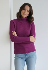 Fuksjowy, prążkowany sweter z golfem i długimi rękawami, noszony z niebieskimi dżinsami; charakteryzuje się dopasowanym krojem i fakturowaną tkaniną.