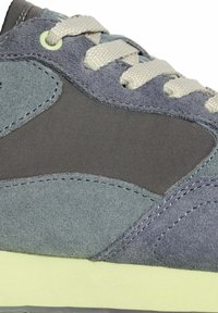 Zapatillas de ante gris con un acento verde apagado, un panel de tela gris suave y cordones en blanco roto. Superficie texturizada con materiales contrastantes.