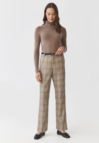 Brązowy sweter z golfem, beżowe spodnie w kratkę, czarny pasek z złotą klamrą oraz czarne płaskie buty. Gładka faktura, dopasowany krój.