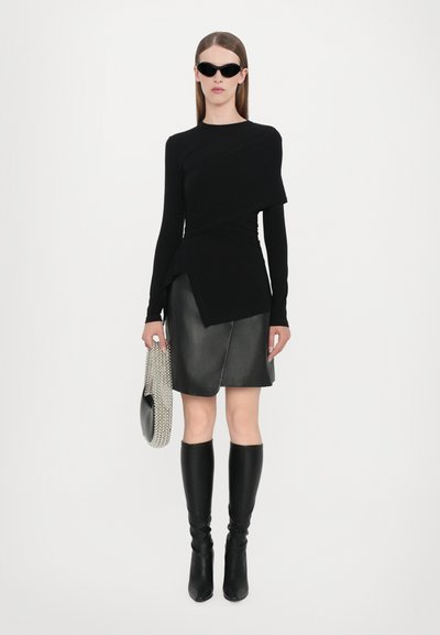 Schwarzes langärmliges Oberteil mit drapiertem Design, kombiniert mit einem schwarzen Leder-Minirock und knielangen schwarzen Stiefeln. Die Accessoires umfassen eine schwarze Tasche und eine Perlenkette.