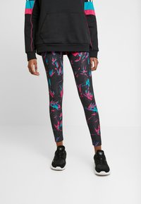 Svarta leggings med ett flerfärgat abstrakt mönster i rosa, turkos och blått; kombinerat med en svart hoodie och svarta sneakers.