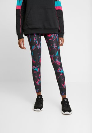 Black leggings with a multicolored abstract pattern in pink, turquoise, and blue; paired with a black hoodie and black sneakers.