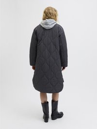 Cappotto lungo, imbottito, di colore grigio scuro con un motivo testurizzato. Presenta un cappuccio grigio e un orlo arrotondato, abbinato a stivali neri al ginocchio.