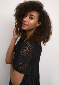 Zwarte kanten jurk met bloemenpatronen, korte mouwen, een ronde halslijn en een geplooide taille. De stof lijkt licht en textuur te hebben.