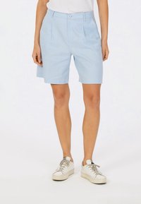 Light blue shorts made of cotton, featuring a button closure, pleats, and a relaxed fit. Paired with white sneakers.