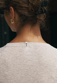 Jasnoszara, prążkowana koszulka z okrągłym dekoltem i małą metką z tyłu, na której jest napisane "self". Krótkie, teksturowane rękawy.