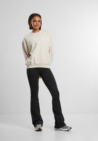 Beige Sweatshirt mit "aim'n"-Text, lässiger Schnitt und gerippte Bündchen, kombiniert mit schwarzen, figurbetonten Hosen, glatter Textur und ausgestelltem Design.