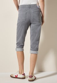 Pantalones de mezclilla gris cortos con puños enrollados, dos bolsillos traseros y una etiqueta en la cintura. Combinados con zapatillas blancas y beige con acentos rojos.