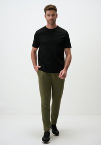 Czarny t-shirt z krótkim rękawem w połączeniu z oliwkowymi spodniami o tapered cut i czarnymi butami sportowymi. Gładki materiał, dopasowany krój, prosta stylizacja.