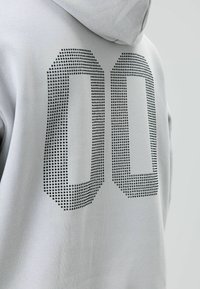 Grijze hoodie met een groot zwart gestippeld nummer "00" op de achterkant gedrukt. Zacht stof met een gladde textuur, verstelbare capuchon.