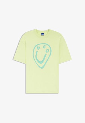 Camiseta de manga corta de color verde claro con un gráfico abstracto azul de una cara sonriente y el texto "HUGO", con una etiqueta de marca azul en el cuello.
