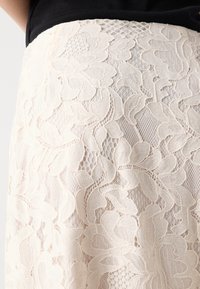 Lace skirt in cream, features floral patterns with intricate detailing, semi-sheer texture, and elastic waistband.