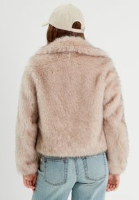 Veste en fausse fourrure rose clair avec un large col et des manches longues, associée à un jean en denim bleu clair. Texture douce et coupe courte.