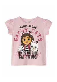 Vaaleanpunainen lyhythihainen t-paita, jossa on sarjakuvahahmoja kissoihin liittyvillä asusteilla, rohkeaa tekstiä ja kimalteita; pehmeä puuvillakangas.