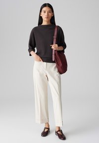 Pull en tricot côtelé noir, pantalon large crème, et sac à épaule bordeaux. Chaussures à enfiler marron avec un détail de boucle.