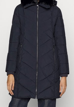 Sort quiltet lang vinterjakke med lynlås foran, lynlåslommer i siden og hætte med kant af sort imiteret pels.