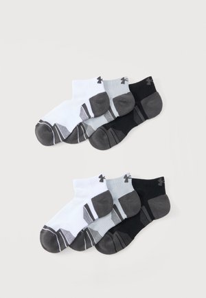 Ensembles de chaussettes courtes en blanc, gris et noir avec des bouts et talons renforcés plus foncés et des motifs rayés, disposés en deux groupes sur un fond clair.
