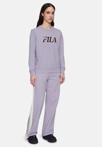 Violetti huppari, jossa on musta ja vaaleanpunainen "FILA"-logo. Yhdistetty yhteensopiviin violetteihin housuihin, joissa on valkoiset sivutähkät. Mustat kengät.