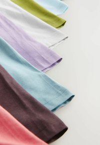 Verschiedene Baumwoll-T-Shirts in Rosa-, Lila-, Grün-, Blau- und Weißtönen, mit hochgerollten Ärmeln und sichtbaren Nähdetails.
