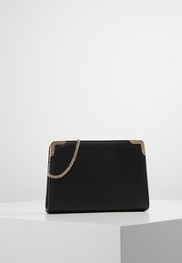 Borsa nera con texture, dettagli in metallo dorato, dotata di una tracolla a catena e una forma rettangolare strutturata. Superfici lisce e linee pulite.