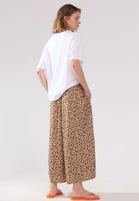 Vit kortärmad skjorta i kombination med bruna leopardmönstrade vida byxor. Outfiten har en avslappnad passform och orangea flip-flops.