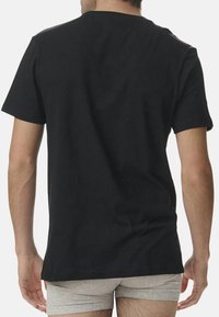 Svart bomullströja med korta ärmar, rund halsringning och en avslappnad passform, visad bakifrån mot en neutral bakgrund.