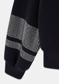 Manche de sweat-shirt noire ornée de grosses strass argentés en rayures horizontales, poignet élastique à l'extrémité, matière en coton doux.