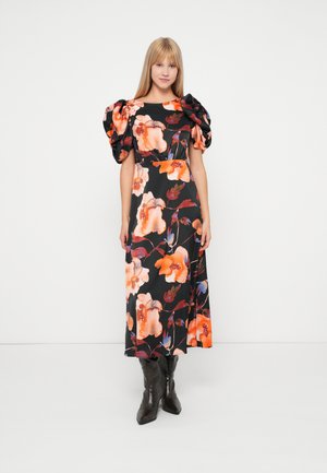 Blomster midi kjole i sort med orange og blå mønstre, der har pufærmer og en indsnøret talje, parret med knæhøje brune støvler.