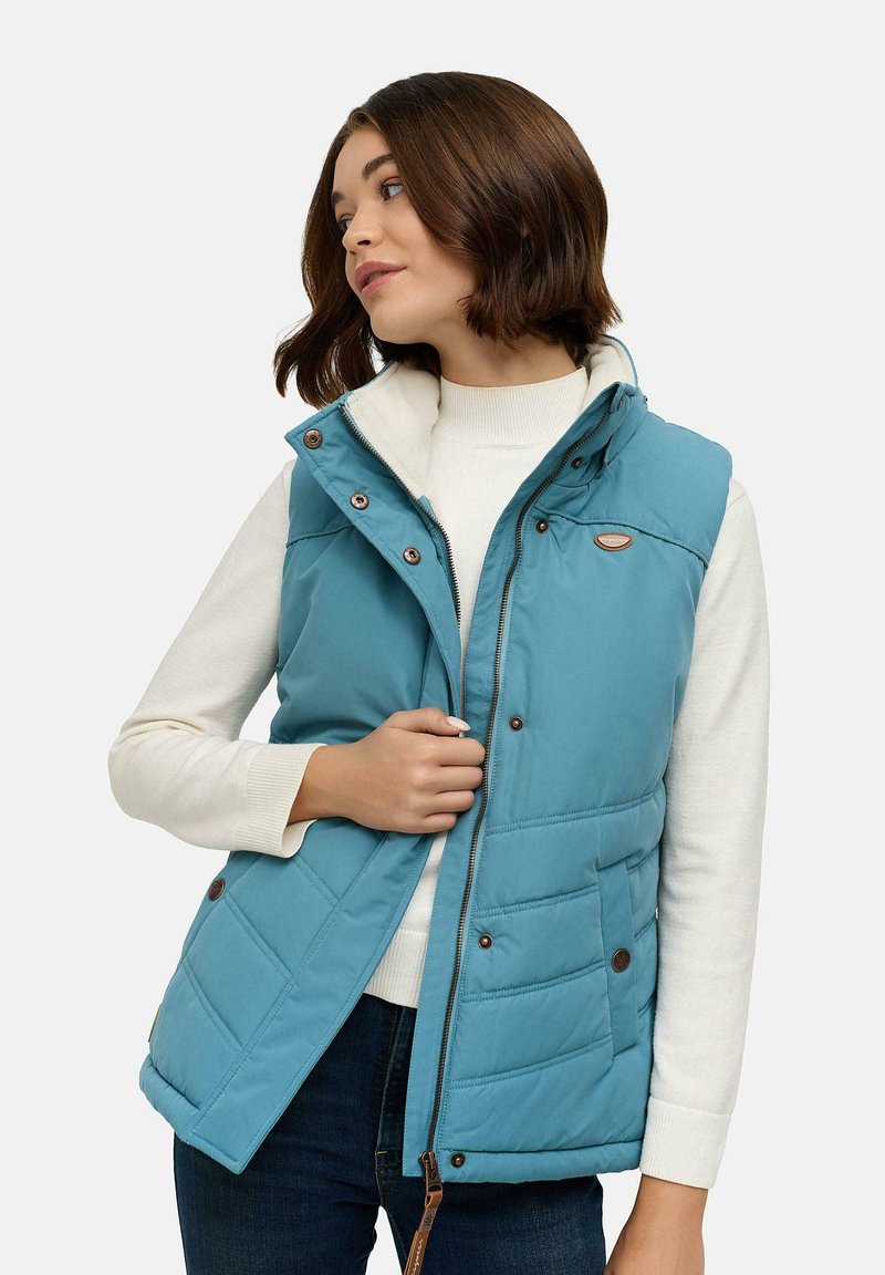 Blue quilted vest with a high collar, front zipper, and snaps. Features two side pockets and a brand logo on the chest. Worn over a white sweater.