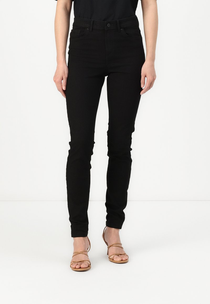 Black skinny jeans with a classic five-pocket design, crafted from denim, featuring belt loops and a zip fly, paired with beige strappy heels.