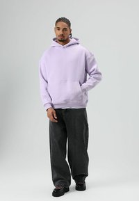 Lavendelkleurige hoodie met een voorzak, oversized pasvorm, geribbelde manchetten en tailleband, gecombineerd met donkergrijze wijde jeans en zwarte schoenen.