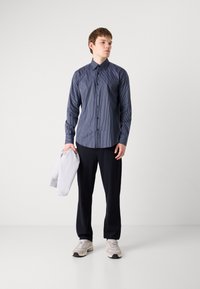 Mørkeblåstripet langermet skjorte, knappedesign, kombinert med mørke bukser og en lysegrå hettegenser hengende over armen.