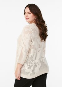 Pull en maille beige clair avec des manches 3/4, présentant un tissage ouvert décoratif et un motif texturé. Poignets et ourlet côtelés.