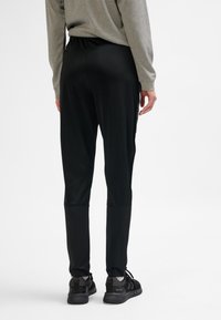 Svarta träningsbyxor i stretchigt material med avsmalnande design och elastisk midja. Matchas med svarta sneakers och en grå långärmad tröja.