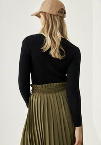 Top negro de manga larga con textura acanalada combinado con una falda plisada color caqui que presenta una cinturilla intrincadamente diseñada y una gorra beige casual.