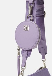 Porte-monnaie rond lilas à fermeture éclair, fixé à une bandoulière ajustable assortie avec des attaches en métal argenté et les initiales "SM" à l'avant.
