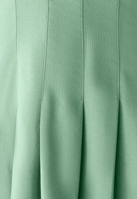 Falda plisada de tejido verde claro con una textura suave. Presenta costuras verticales que van desde la cinturilla para añadir estructura.