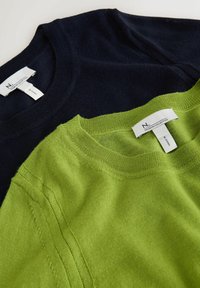 Două pulovere așezate unul peste altul: unul de culoare bleumarin și unul de culoare verde aprins. Ambele au decolteu rotund și o textură moale, fină, cu etichete vizibile.